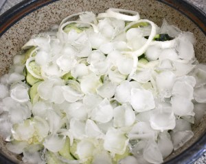 The first step in making bread and butter pickles is to slice cucumbers and onions and let them sit with salt and ice for two hours.